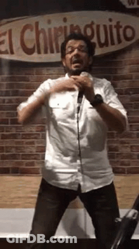 A Man In A White Shirt Is Standing In Front Of A Microphone And Singing Into It . GIF
