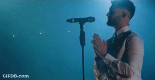 A Man In A White Shirt Is Standing In Front Of A Microphone Covering His Face . GIF