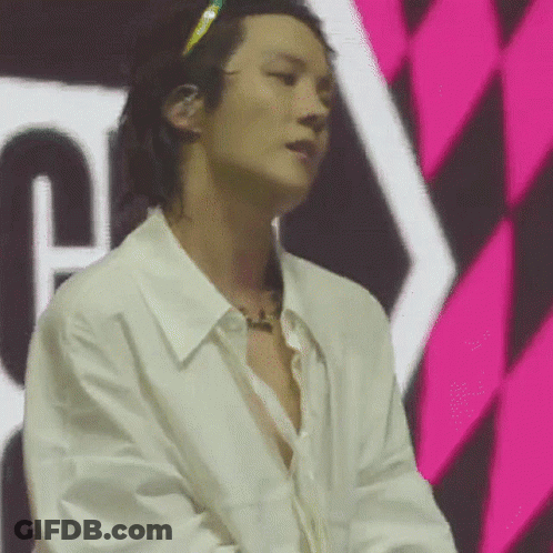 A Man In A White Shirt Is Standing In Front Of A Pink And Black Checkered Wall . GIF