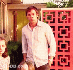 A Man In A White Shirt Is Standing In Front Of A Pink Fence GIF