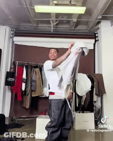 Man In White Shirt Holding Shirt In Front Of Clothes Rack GIF