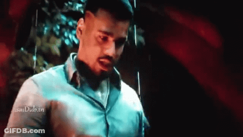 A Man In A White Shirt Is Standing In Front Of A Red Wall And Talking To Someone . GIF