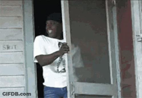 A Man In A White Shirt Is Standing In Front Of A Screen Door Holding A Drink . GIF