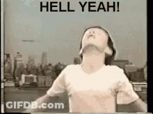 A Man In A White Shirt Is Standing In Front Of A Sign That Says Hell Yeah . GIF