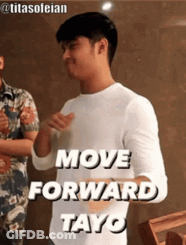 A Man In A White Shirt Is Standing In Front Of A Sign That Says `` Move Forward Tayo '' . GIF
