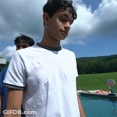 A Man In A White Shirt Is Standing In Front Of A Swimming Pool GIF
