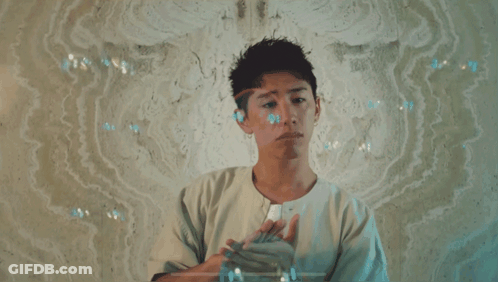 A Man In A White Shirt Is Standing In Front Of A Wall With Bubbles Coming Out Of It GIF