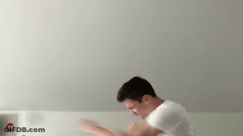 A Man In A White Shirt Is Standing In Front Of A White Wall With A Red Sign That Says ' Aa ' GIF