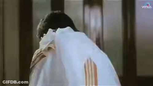 A Man In A White Shirt Is Standing In Front Of A Window And Looking Down . GIF