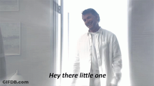 A Man In A White Shirt Is Standing In Front Of A Window With The Words Hey There Little One Below Him GIF