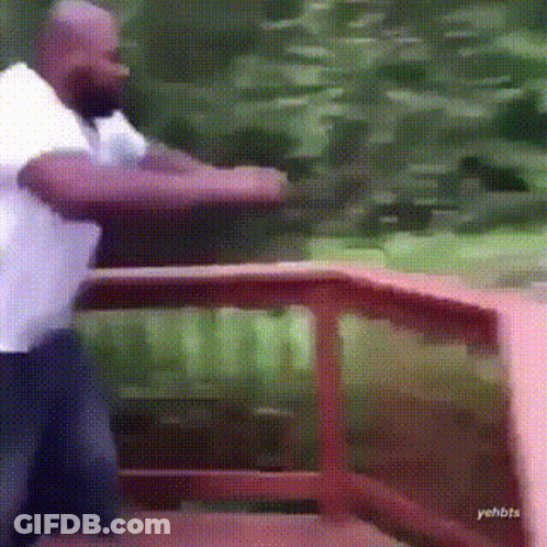 A Man In A White Shirt Is Standing In Front Of A Wooden Railing . GIF