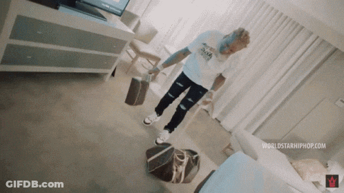 A Man In A White Shirt Is Standing On A Bag In A Room GIF