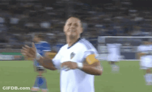 A Man In A White Shirt Is Standing On A Soccer Field With His Hands In The Air GIF