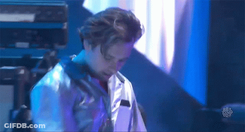 A Man In A White Shirt Is Standing On A Stage In Front Of A Blue Light . GIF
