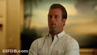 A Man In A White Shirt Is Standing With His Arms Crossed And Looking At The Camera . GIF