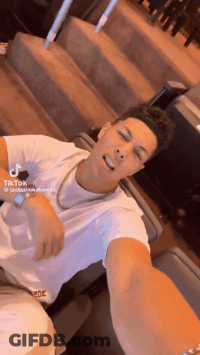 A Man In A White Shirt Is Taking A Selfie While Wearing A Gold Chain Around His Neck . GIF