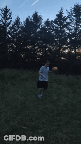 A Man In A White Shirt Is Throwing A Frisbee In A Field With Trees In The Background GIF