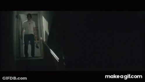 A Man In A White Shirt Is Walking Down A Set Of Stairs With A Knife In His Hand . GIF