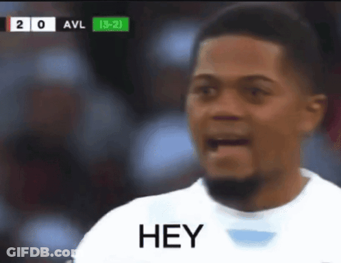 A Man In A White Shirt Says Hey In Front Of A Scoreboard GIF