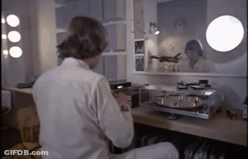 A Man In A White Shirt Sits At A Table In Front Of A Mirror With The Word Gf On It GIF