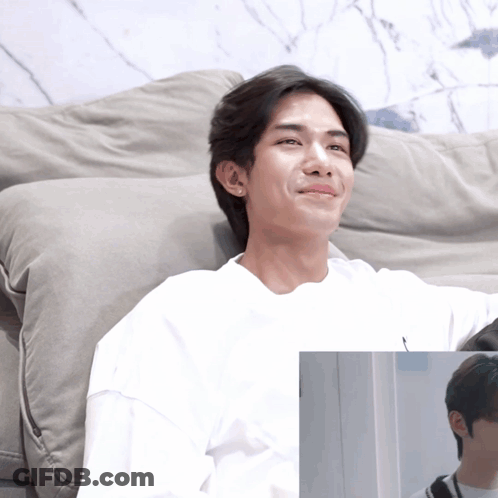 A Man In A White Shirt Sits On A Grey Couch GIF