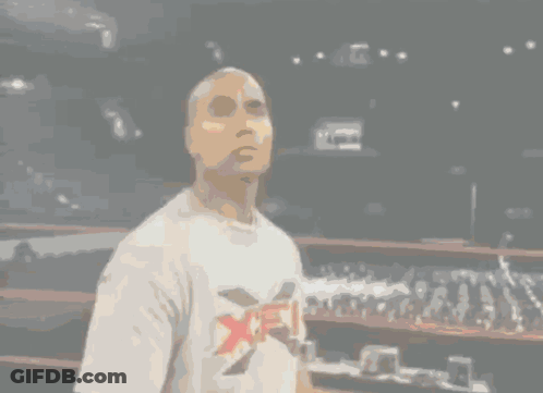 A Man In A White Shirt Stands In A Dark Room GIF