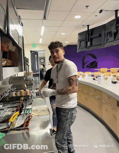 A Man In A White Shirt Stands In A Kitchen With A Taco Bell Logo In The Background GIF