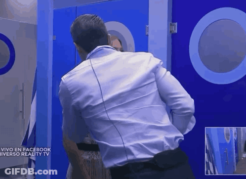 A Man In A White Shirt Stands In Front Of A Blue Door That Says Vivo En Facebook Universo Reality TV GIF