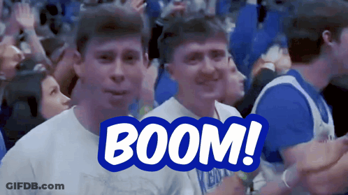 A Man In A White Shirt Stands In Front Of A Blue Sign That Reads Boom GIF