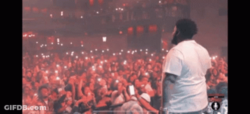 A Man In A White Shirt Stands In Front Of A Large Crowd GIF