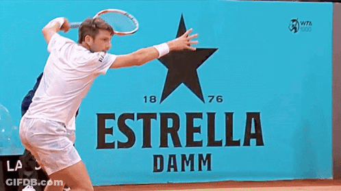 A Man In A White Shirt Stands In Front Of A Sign That Says Estrella Damm GIF