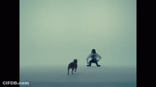 A Man In A White Shirt With A Cross On It Stands Next To A Dog GIF
