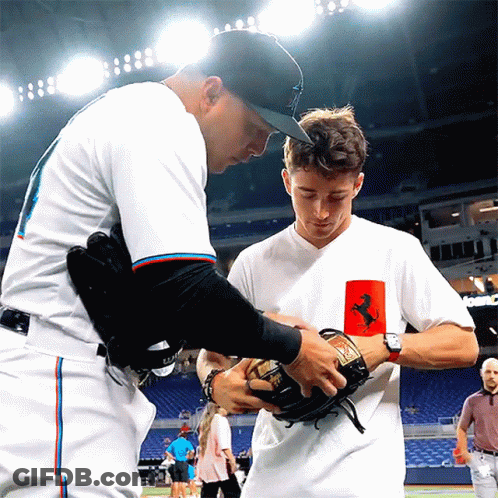 A Man In A White Shirt With A Ferrari Logo On It Talks To Another Man GIF