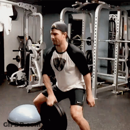 A Man In A White Shirt With The Word Mustang On It Is Squatting GIF
