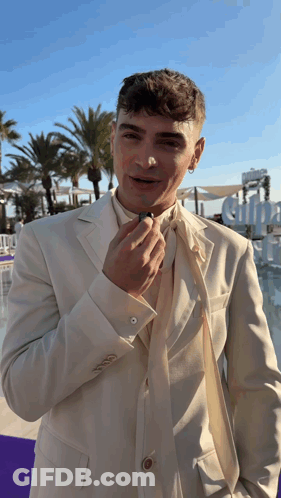 A Man In A White Suit Adjusts His Tie In Front Of A Sign That Says Alpha GIF