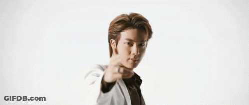 A Man In A White Suit And Black Shirt Is Standing In Front Of A White Wall . GIF