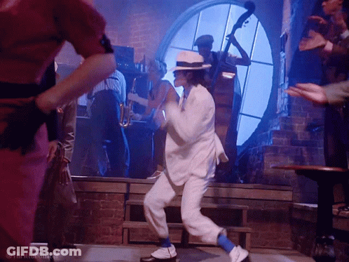 A Man In A White Suit And Blue Socks Is Dancing In Front Of A Group Of People GIF