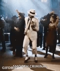 A Man In A White Suit And Hat Is Dancing In Front Of A Crowd At A Party . GIF