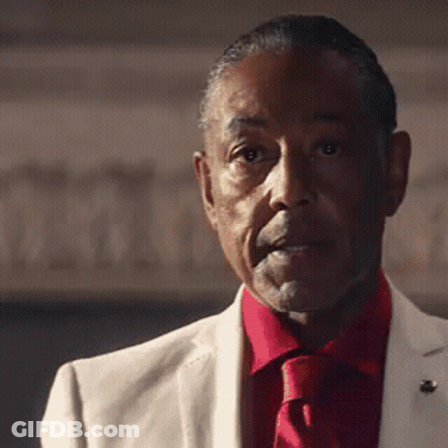 A Man In A White Suit And Red Tie Is Looking At The Camera GIF