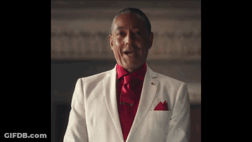 A Man In A White Suit And Red Tie Is Standing In A Room . GIF