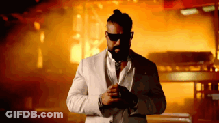 A Man In A White Suit And Sunglasses Stands In Front Of A Fire GIF