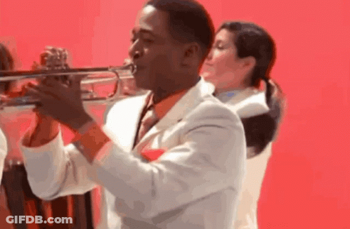 A Man In A White Suit And Tie Is Playing A Trumpet GIF