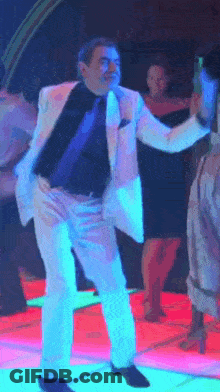 A Man In A White Suit Is Dancing On A Neon Dance Floor GIF