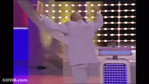 A Man In A White Suit Is Dancing On A Stage With His Arms Outstretched . GIF