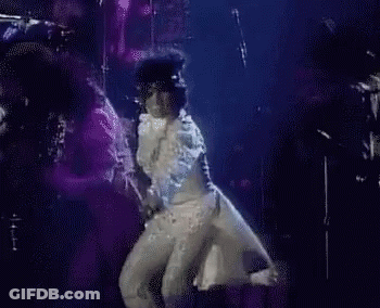 A Man In A White Suit Is Dancing On A Stage . GIF