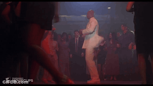 A Man In A White Suit Is Dancing With A Woman In An Orange Dress At A Party GIF