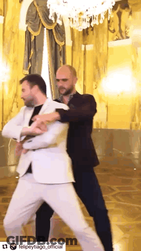 A Man In A White Suit Is Dancing With Another Man In Black Pants GIF