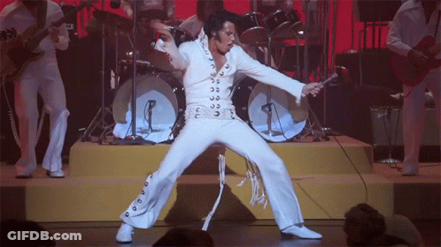 A Man In A White Suit Is Holding A Microphone And Dancing On Stage GIF