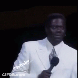 A Man In A White Suit Is Holding A Microphone In His Hand . GIF