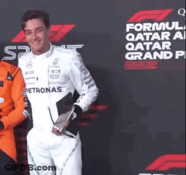 A Man In A White Suit Is Holding A Trophy In Front Of A Sign That Says Formula 1 Qatar Grand Prix . GIF